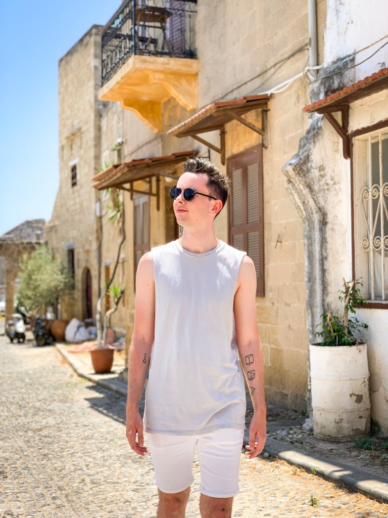 A man in a vest top walks old cobbled streets of Old Town Rhodes 
